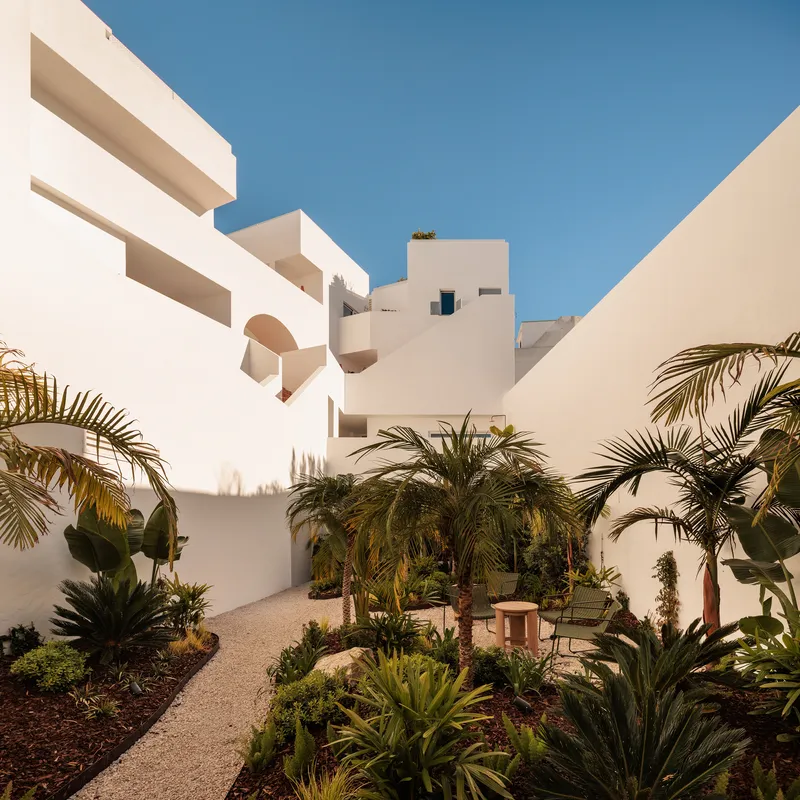 Garden courtyard with white stepped volumes, gravel path and palm plantings under clear blue sky