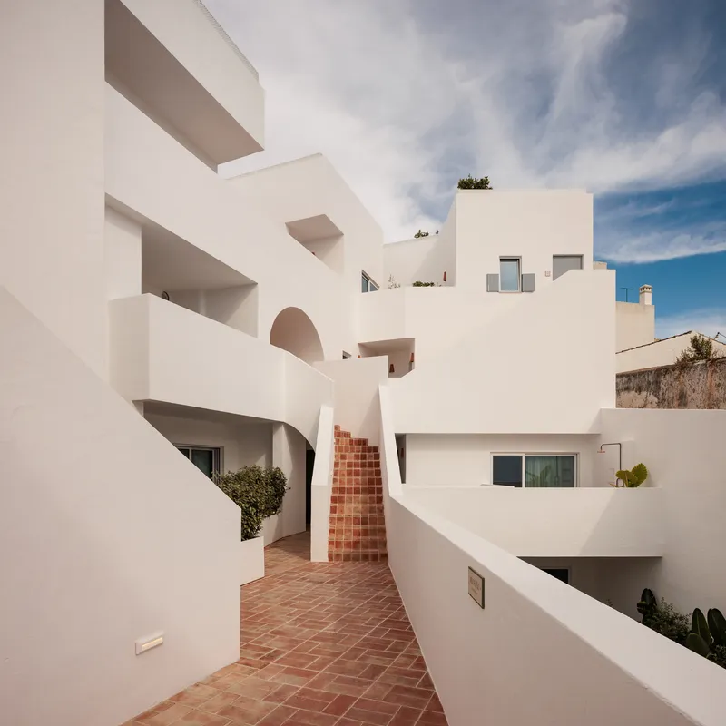 White-rendered facade with terracotta brick staircase and terracotta paving under a clear blue sky
