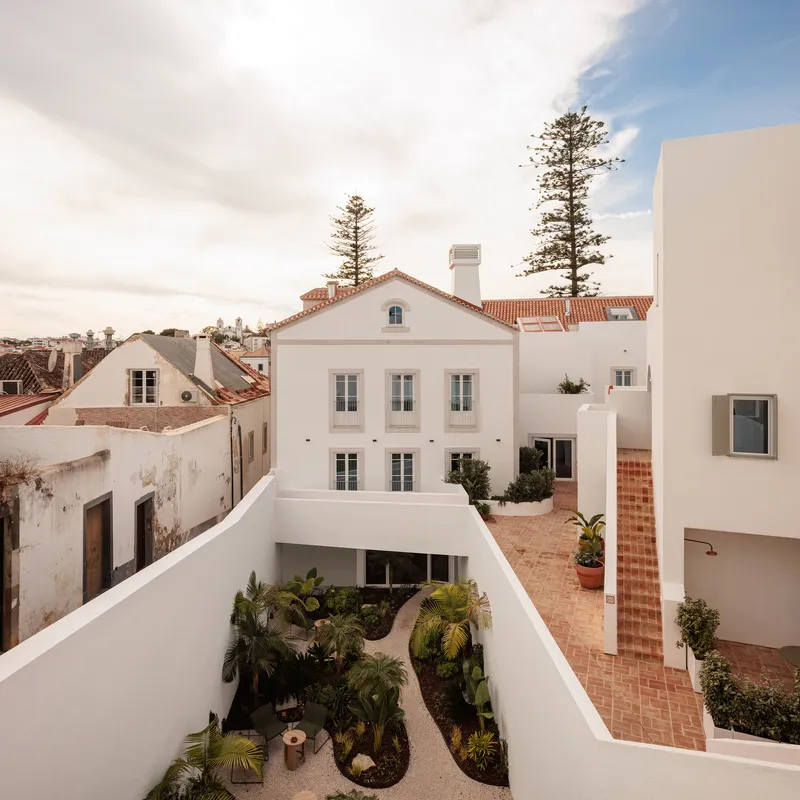 Courtyard with planted beds and terracotta paving overlooking a traditional tile-roofed building beyond