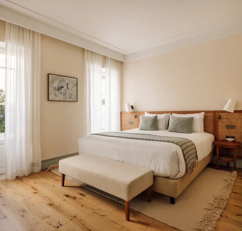 Bedroom with timber headboard, knotted pine flooring and sheer curtains filtering daylight