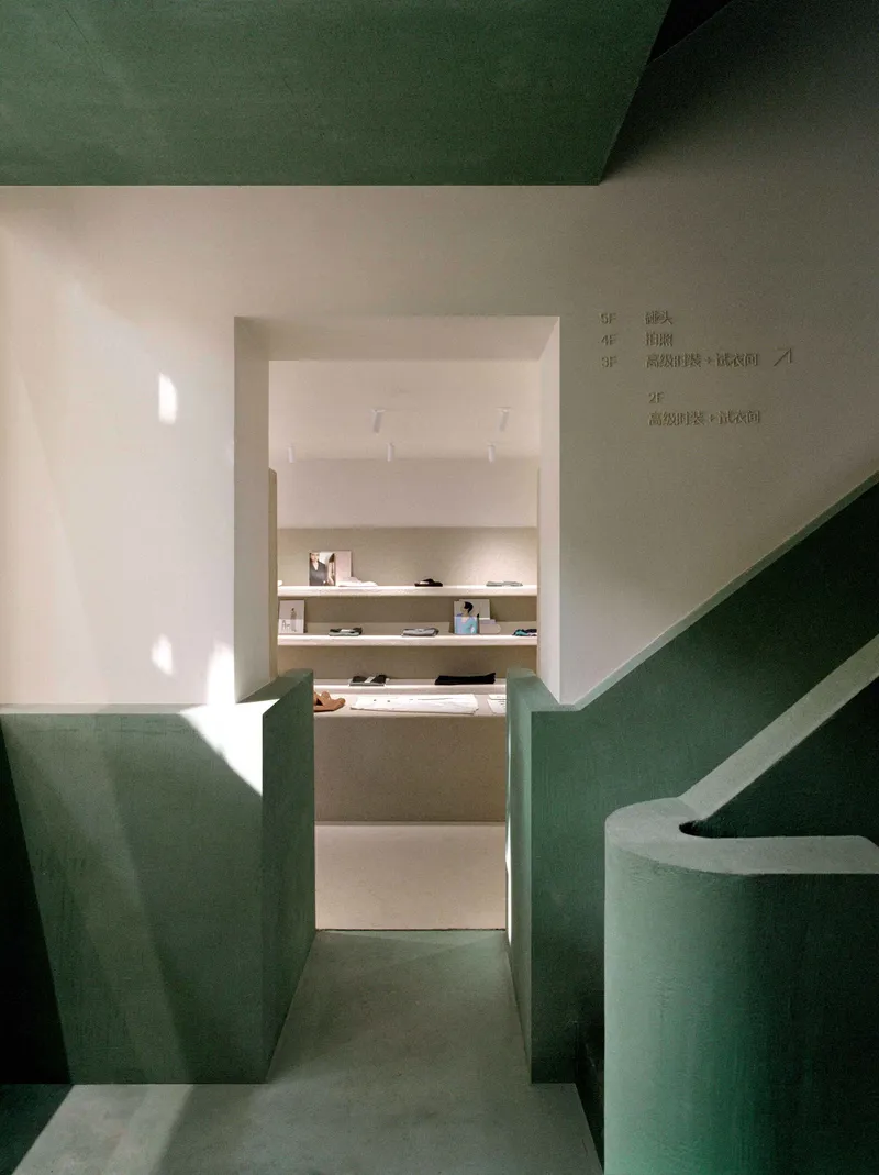 Narrow corridor between green plastered walls leading to a white display room with shelving
