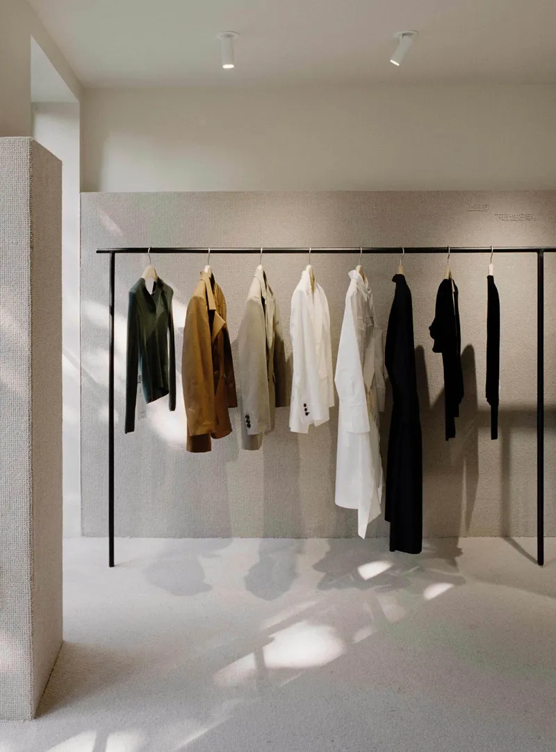 Black clothing rail with hanging garments in natural light against textured plaster wall