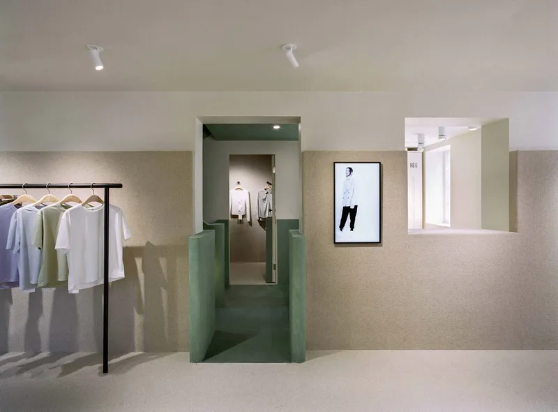 Retail interior with green plaster portal framing a corridor and clothing rack along textured beige walls