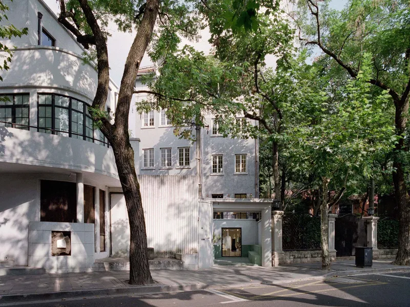 Street view of white facade insertion between historic buildings framed by mature deciduous trees