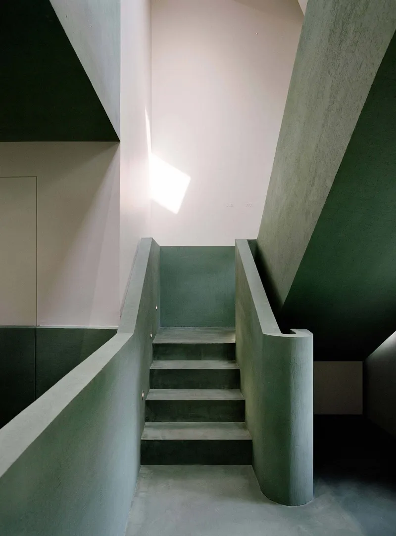 Stairwell with green plaster walls and cylindrical column rising to a skylight above