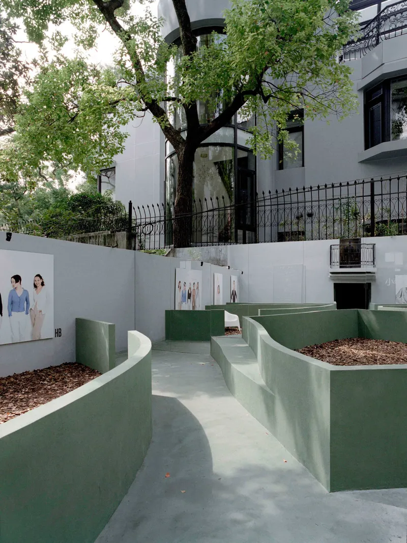 Curving sage green planters with mulch beds and concrete walkways below a preserved tree