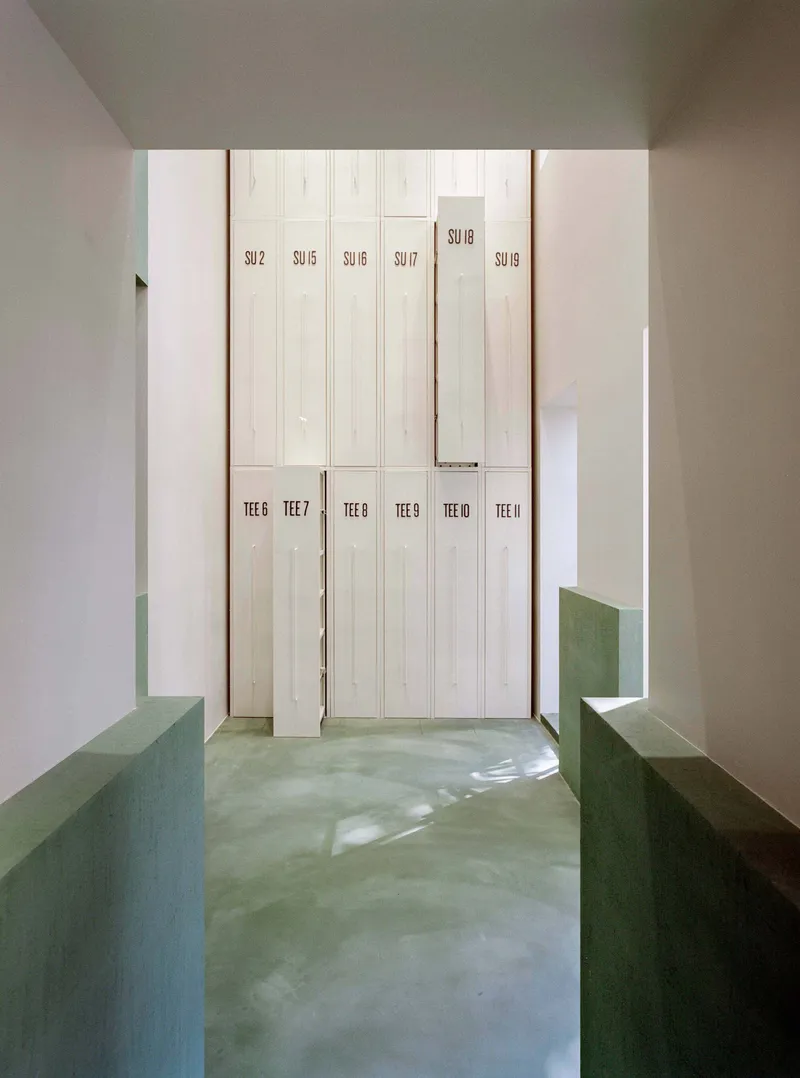 View through green concrete benches toward tall white storage lockers with numbered labels