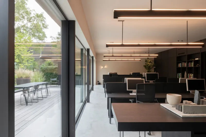 Office interior with black workstations and suspended linear lighting opening to a timber deck terrace