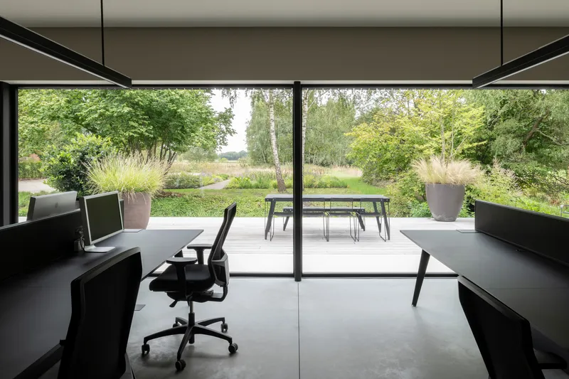 Workspace with floor-to-ceiling glazing framing views of the grassy landscape and outdoor dining area