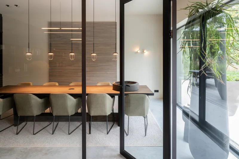 Glass-paneled sliding door revealing the dining room with timber table and horizontal slatted screens