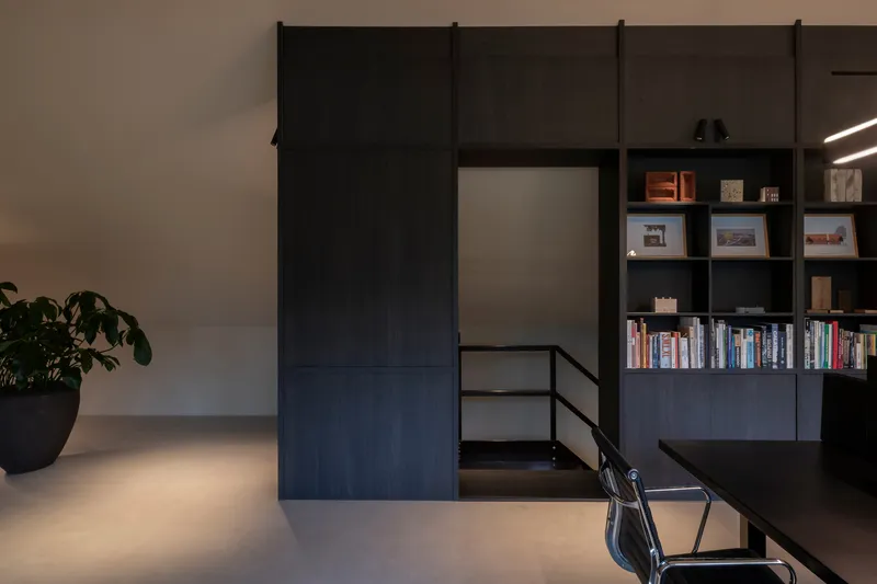 Black sliding barn door on steel track beside built-in shelving and polished concrete floor