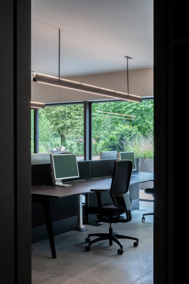 Office desk framed by doorway with suspended linear lighting and garden view beyond