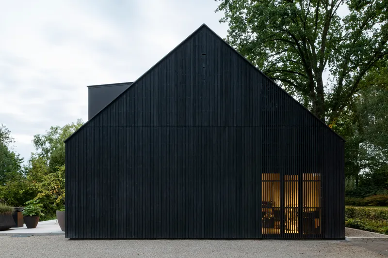 Gable end of black vertical timber cladding with backlit timber screen at entry under an overcast sky