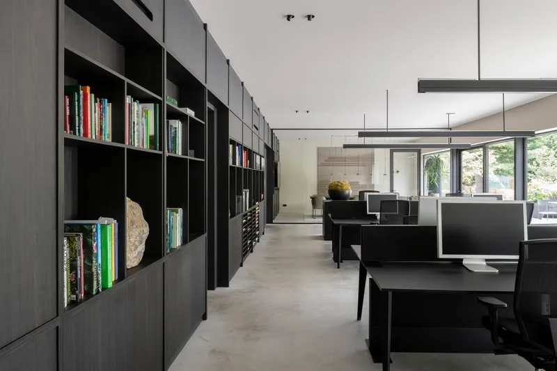 Open office interior with black modular shelving along one wall and workstations beneath linear pendant lights