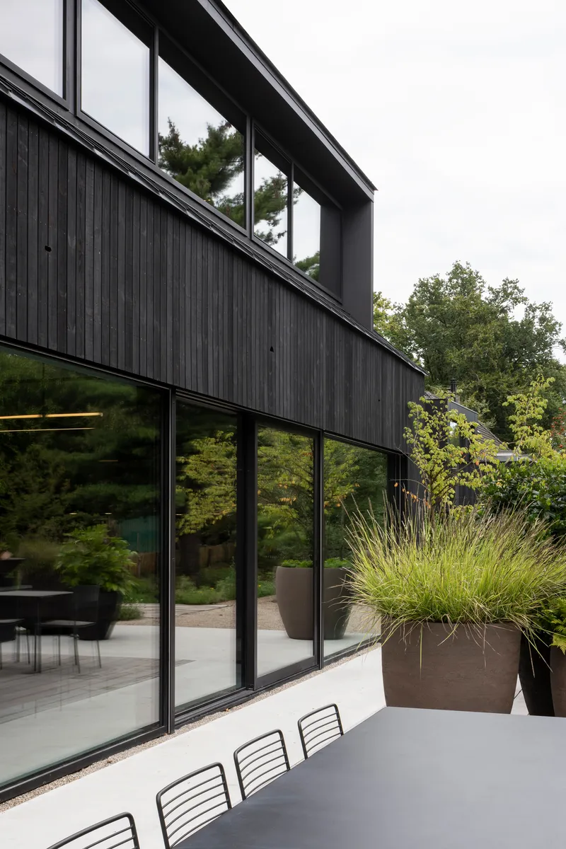 Corner facade detail showing vertically clad upper volume with clerestory windows above continuous ground floor glazing and planted containers