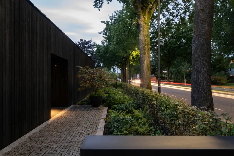 Street view of the entrance path and timber screen with vehicle light trails at twilight