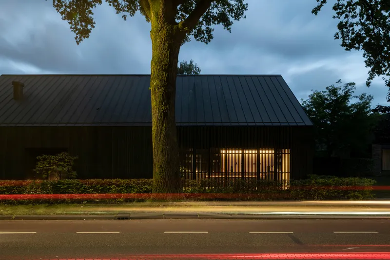 Street elevation with vertical slatted screen and pitched metal roof at dusk with passing traffic