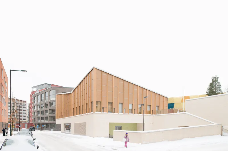 Street corner view of the vertical timber-clad facade atop white concrete walls in fresh snow