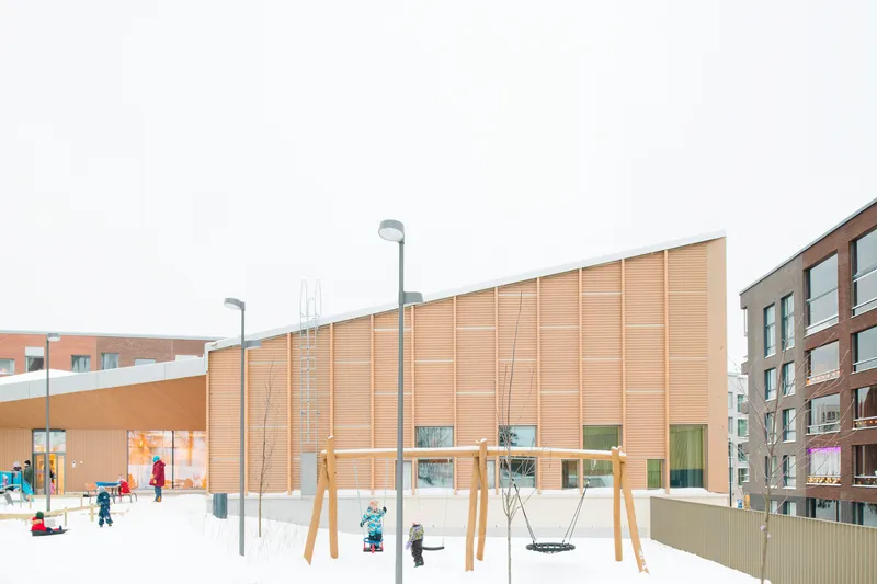 Timber facade with ground-level glazing overlooking a snow-covered playground with children and swings