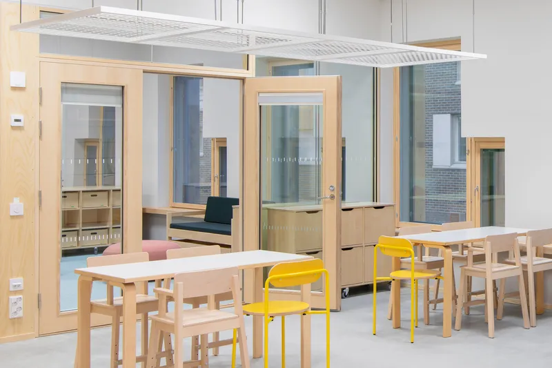Interior space with timber tables, yellow metal chairs, and glazed partitions under a white canopy