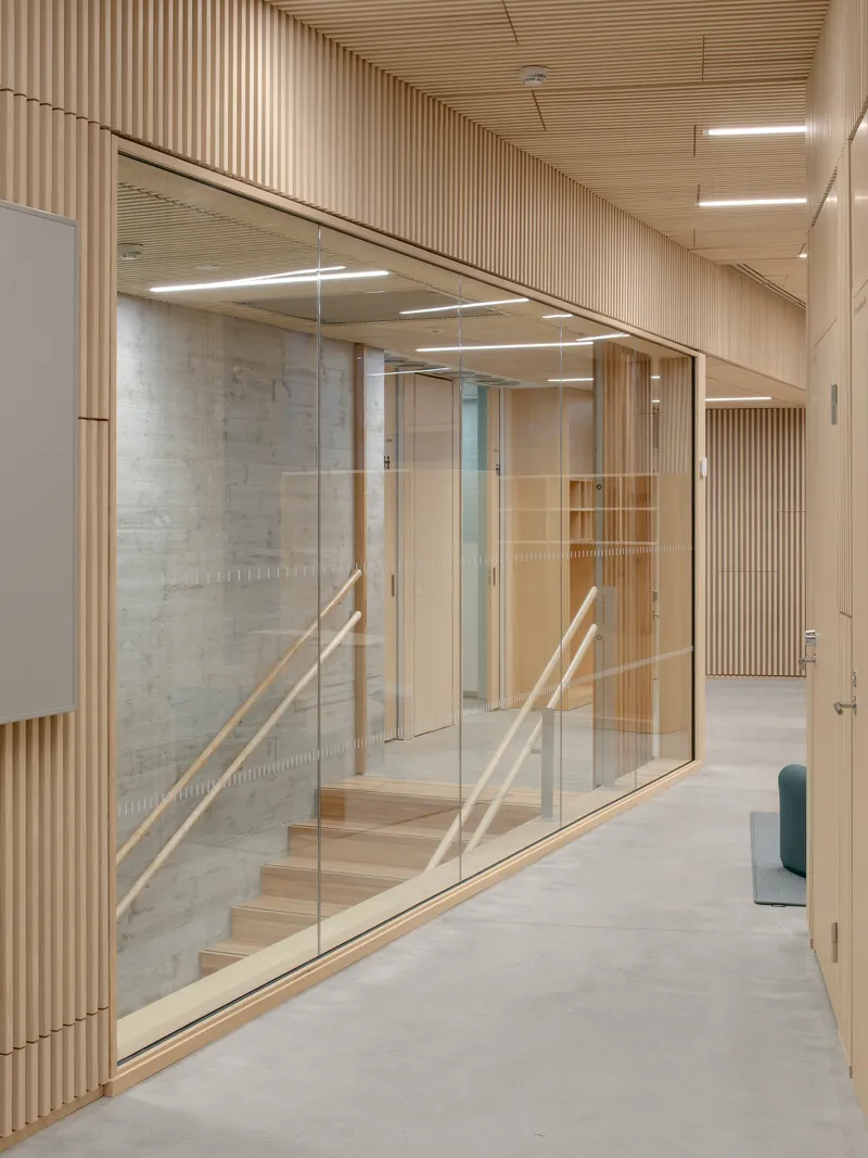 Glass-enclosed stairwell visible through floor-to-ceiling glazing along a slatted wood corridor