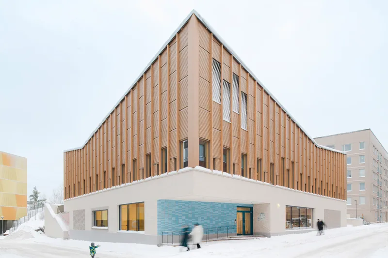 Corner view of the two-story facade with vertical timber cladding above a white base and blue tiled entry in fresh snow