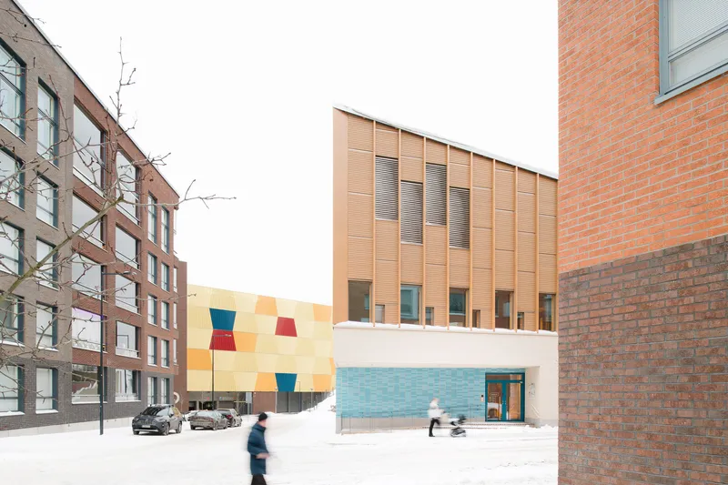 Street view showing the timber facade and colorful tiled wall between residential buildings with pedestrians in winter