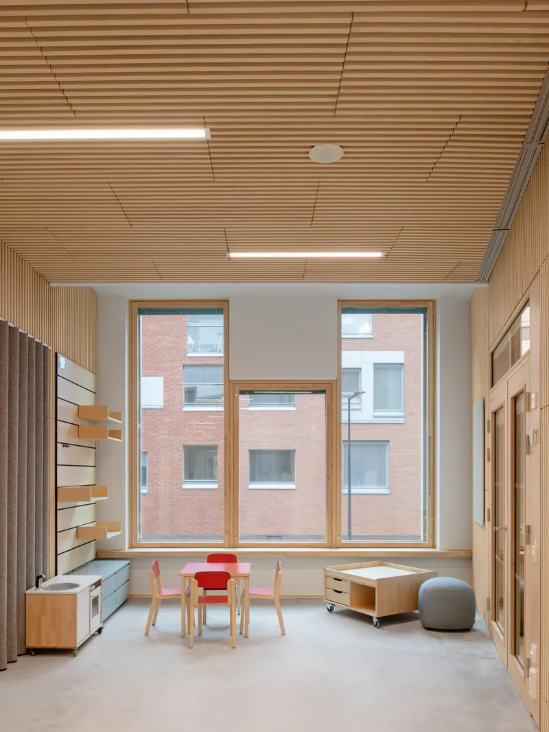 Interior room with slatted timber ceiling, floor-to-ceiling windows, and light wood furniture under recessed linear lighting