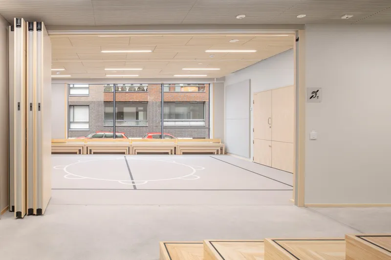 Multipurpose interior space with folding partitions, timber benches, and acoustic ceiling panels under fluorescent lights