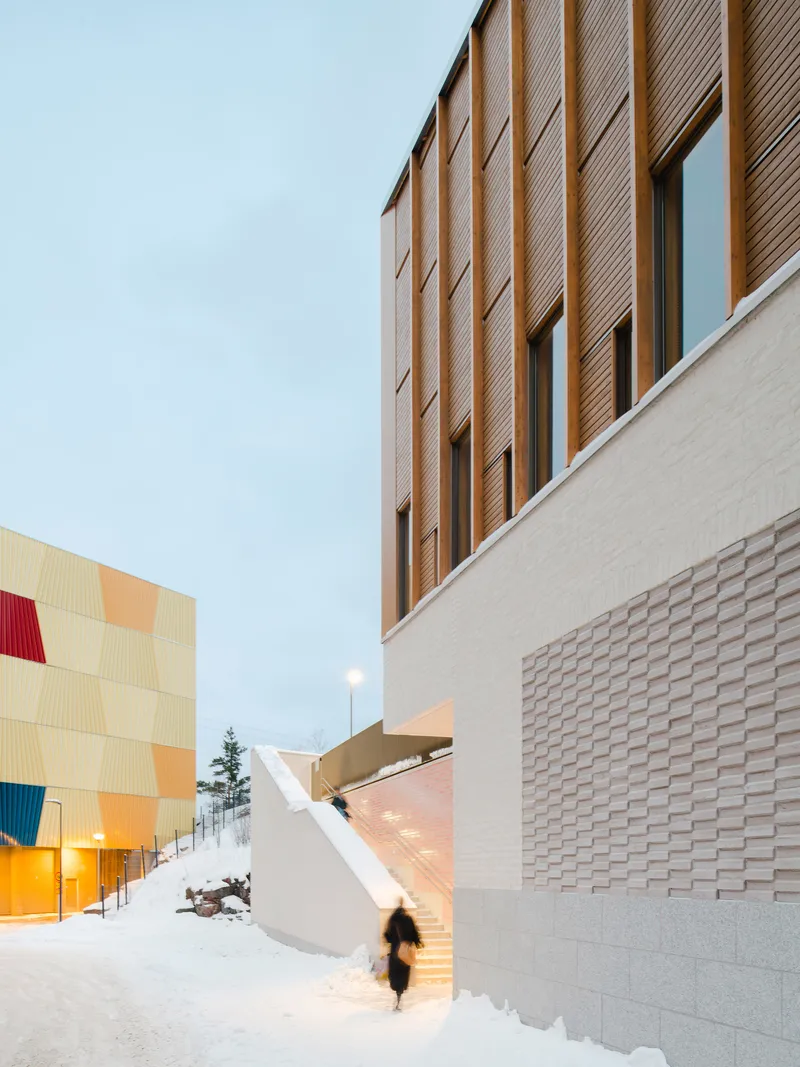 Exterior passage between textured brick base and vertical wood cladding during winter twilight