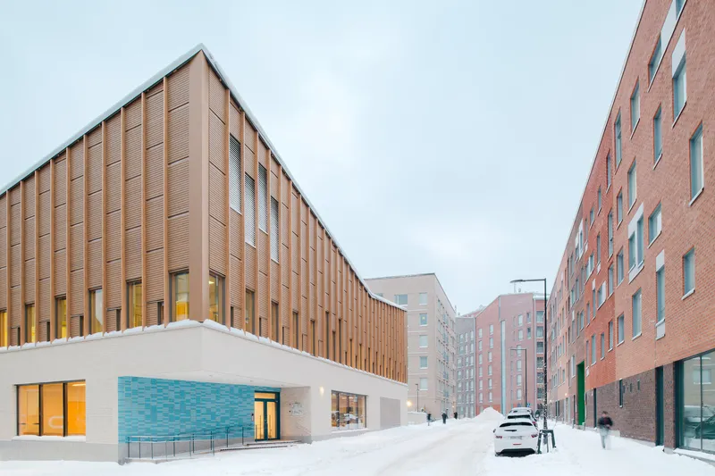 Corner facade with vertical wood slat cladding meeting white brick and turquoise tile under overcast sky