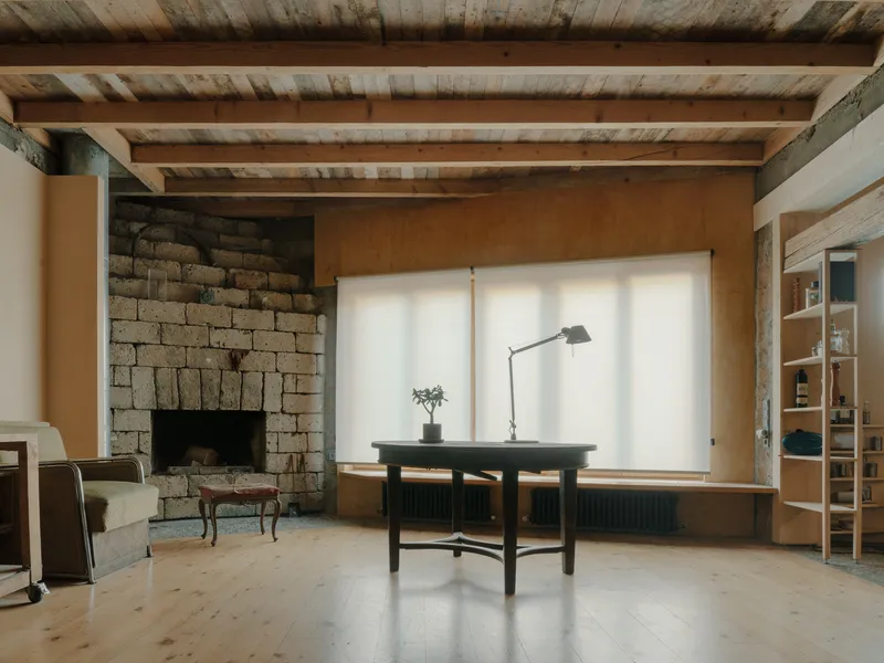 Interior with exposed timber beam ceiling, stone fireplace and black desk beneath diffused window light