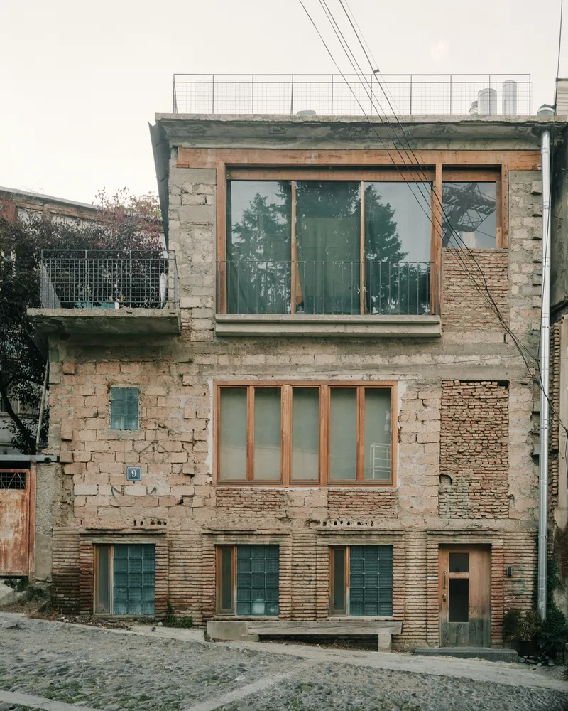 Street facade with stacked stone and brick volumes, timber-framed glazing and overhead power lines