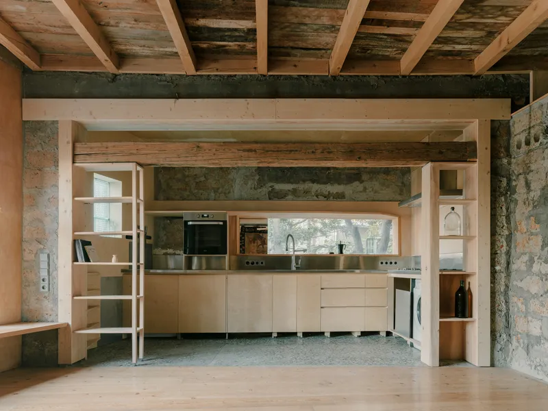 Timber-framed kitchen alcove with plywood cabinetry set within exposed masonry walls and beamed ceiling