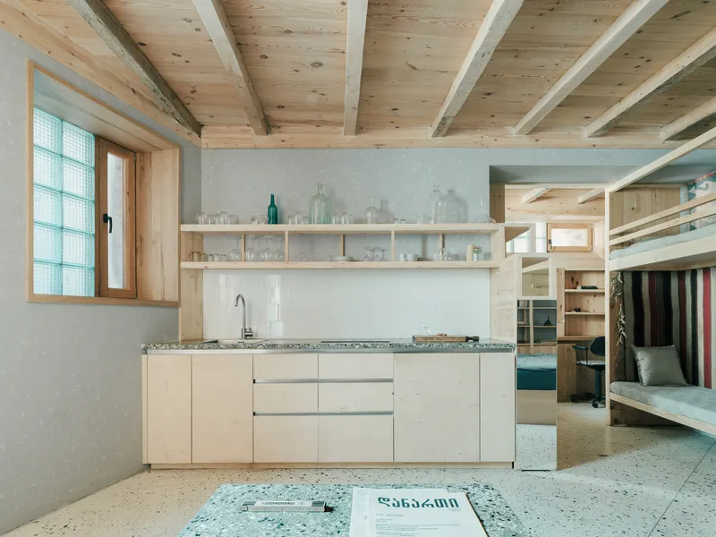 Kitchen with pale wood cabinetry and terrazzo floor beneath exposed timber beam ceiling