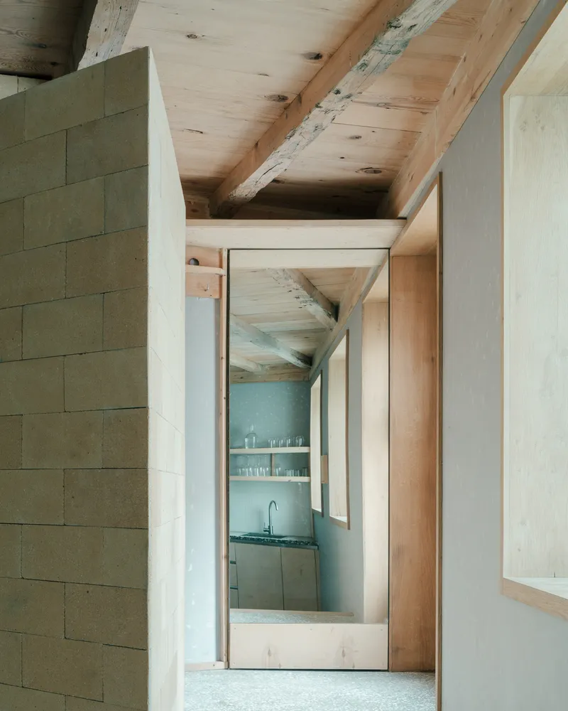 Interior passage with timber doorframe and glimpse of kitchen beyond plaster walls