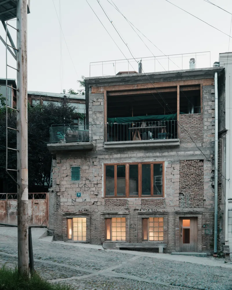 Three-story facade mixing concrete block, exposed brick, and timber fenestration at dusk