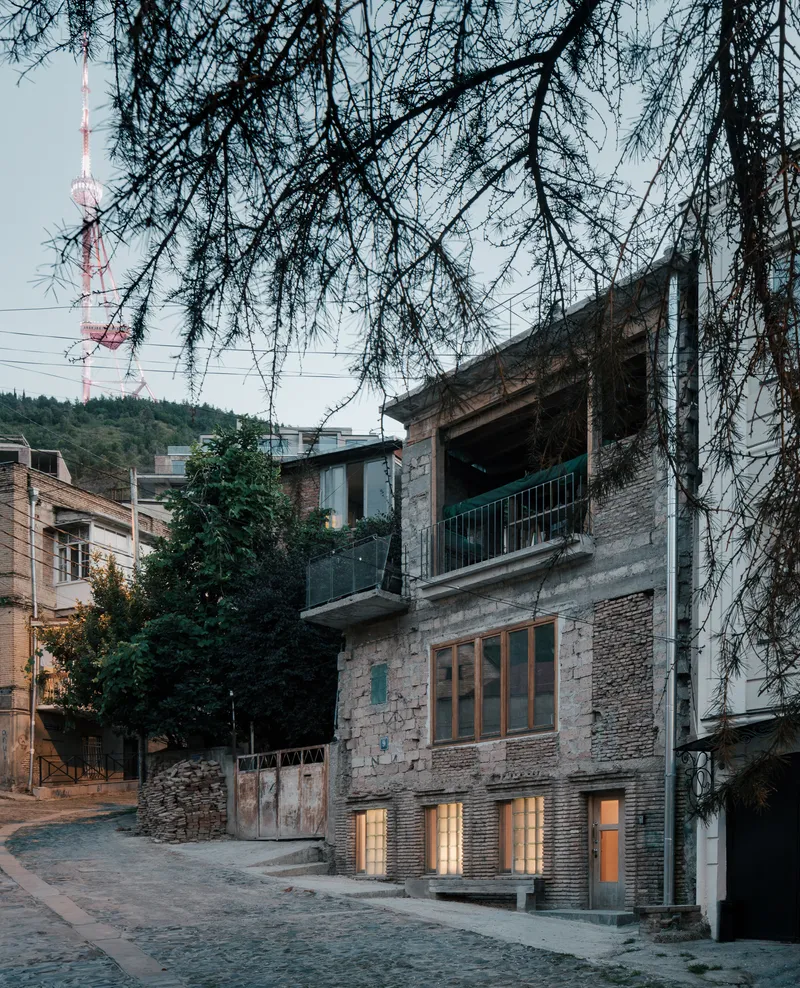Street view of the brick facade with illuminated ground floor openings at dusk beneath bare tree branches