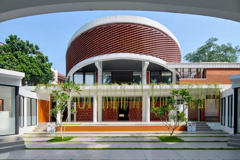 Courtyard view of curved brick drum above planted terrace with hanging greenery and columned walkways
