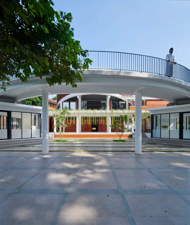 Curved cantilevered terrace with metal railing and person standing above planted ground plane with trees