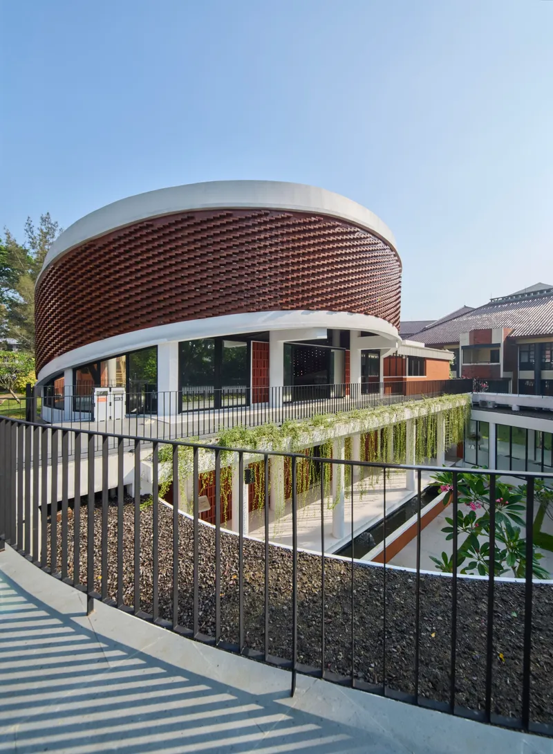 Curved staircase with metal railing leading to planted terrace below cylindrical basketweave brick facade
