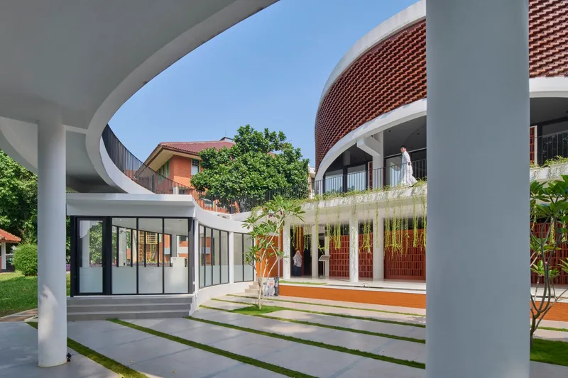 View through white columns framing courtyard with grass strips and person on upper terrace