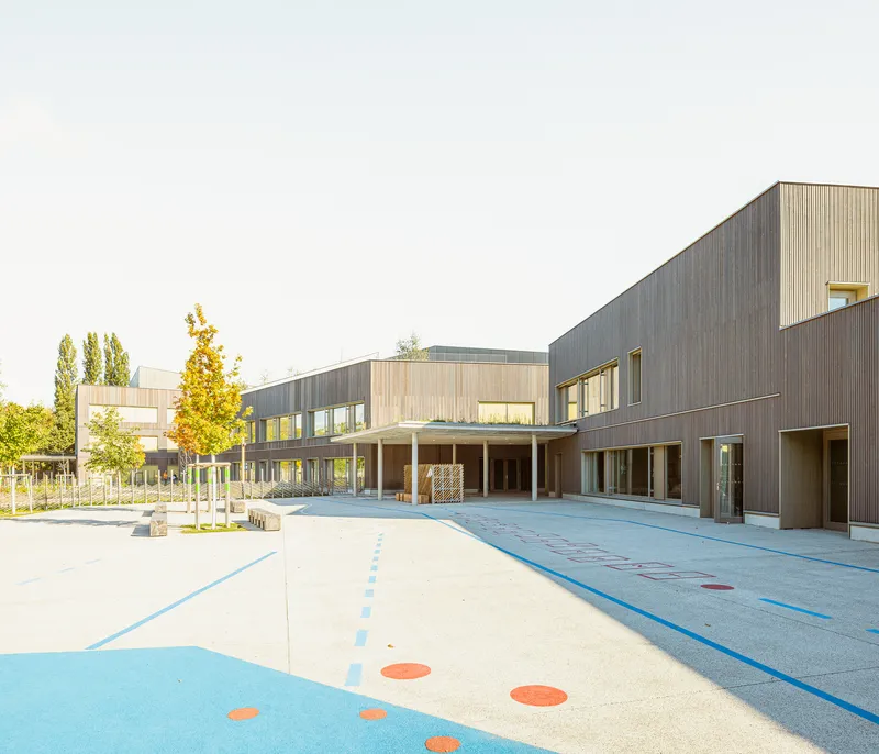 Courtyard view of the vertically ribbed timber facade with colored pavement markings in the foreground