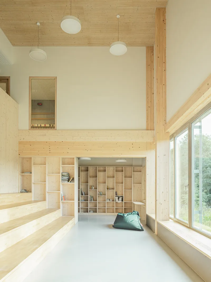 Reading nook with grid shelving beneath a timber mezzanine and floor cushion on pale flooring