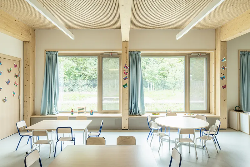 Classroom interior with timber columns, slatted ceiling, large windows overlooking green landscape and round tables