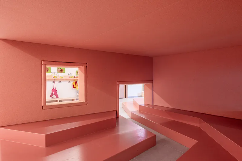 Coral-pink room with built-in stepped seating platforms and window openings framing adjacent spaces