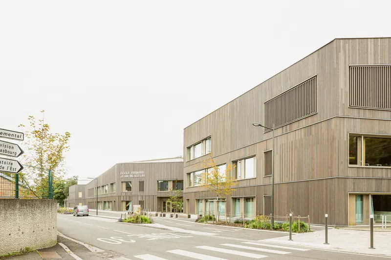 Street view of the weathered timber facade with vertical screen panels and roadside bollards