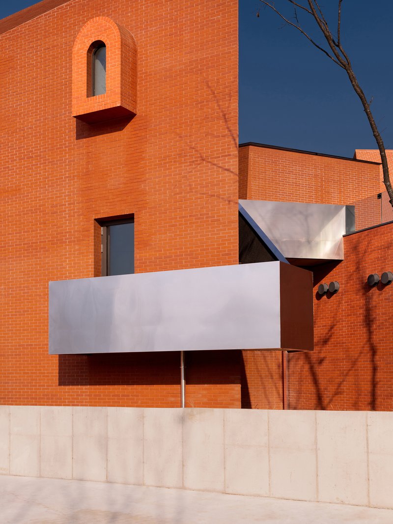 Orange brick facade with white metal canopies and an arched window opening above clear sky