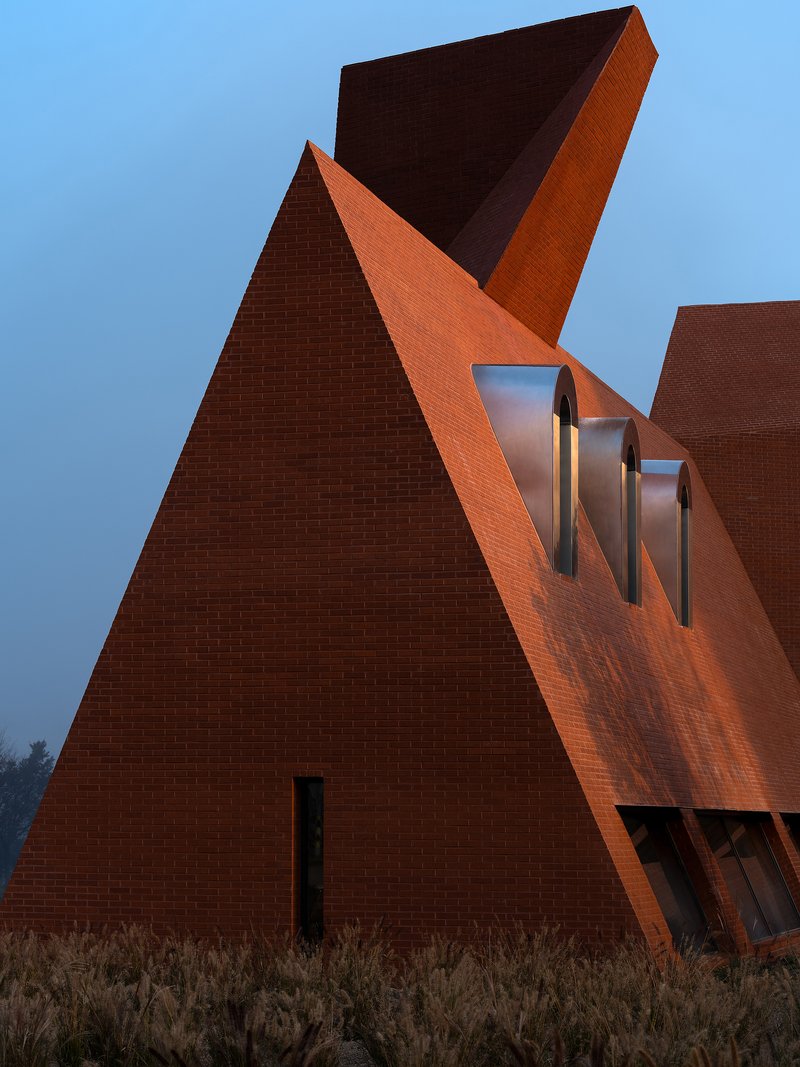 Red brick facade with triangular forms and curved dormer windows at dusk