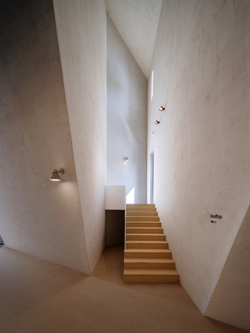 Timber staircase rising between angled white plaster walls with skylight above